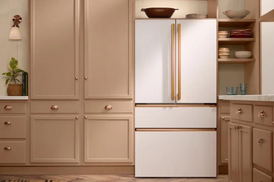 French door refrigerator in a matte white finish with brass vertical bar handles, built into blush-toned cabinetry with brass hardware.