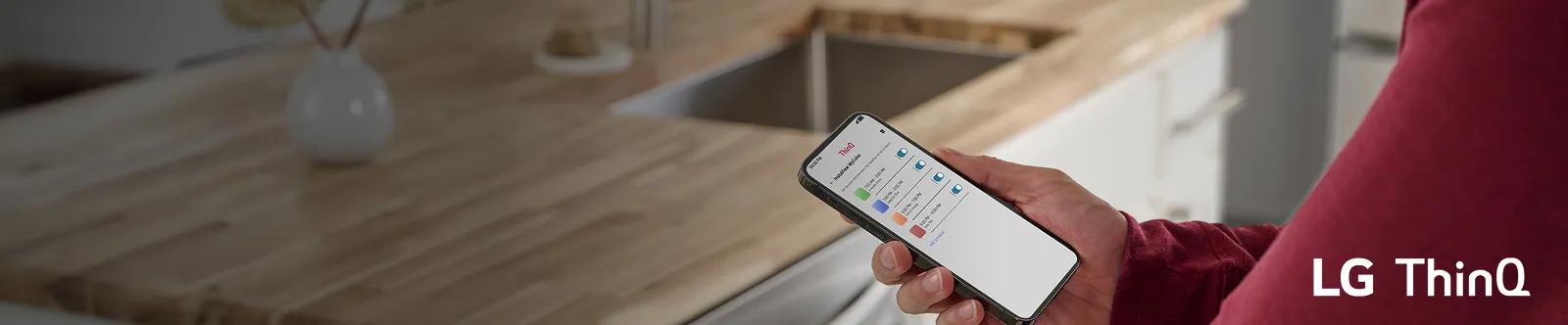 Person holding a smartphone in a kitchen while using the LG ThinQ app, which shows the app’s MyColor schedule and color settings.