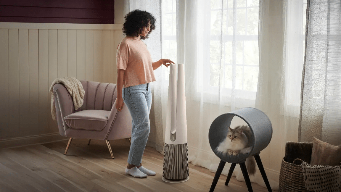 A woman adjusts her PuriCare™ air purifier in a sun-filled room. 