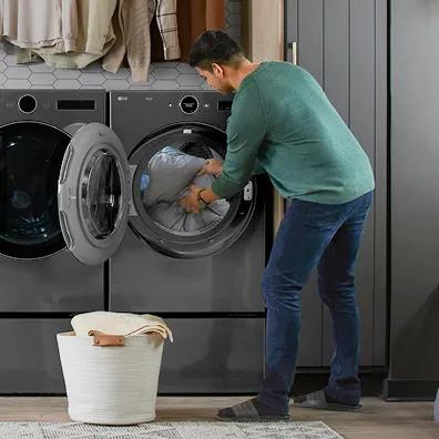 A man empties blankets and linens into a laundry basket from an LG front load dryer.
