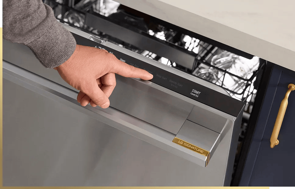 Close-up of a hand pressing the control panel on an LG SIGNATURE dishwasher with door open and dishes visible inside.