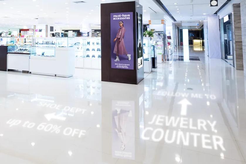 The interior of a department store, featuring LG digital signage advertising sales, and projected wayfinding directions pointing customers to various sales and departments. 