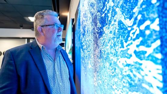 A man wearing business casual looking at an LG Direct View LED display. He's close enough for the display's vivid colors to reflect off of him, casting a blue glow over him. 