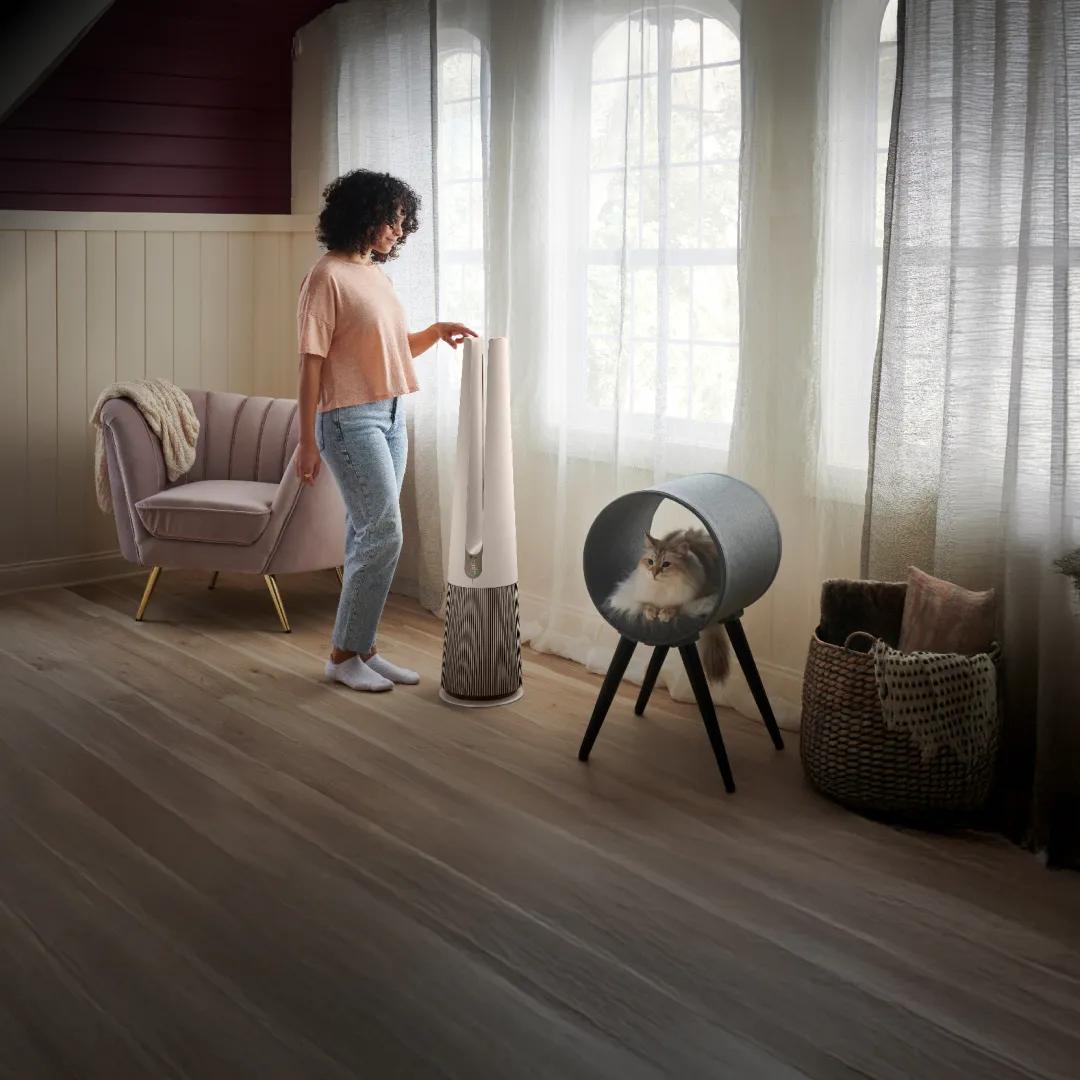 A woman adjusts her PuriCare™ air purifier in a sun-filled room. 