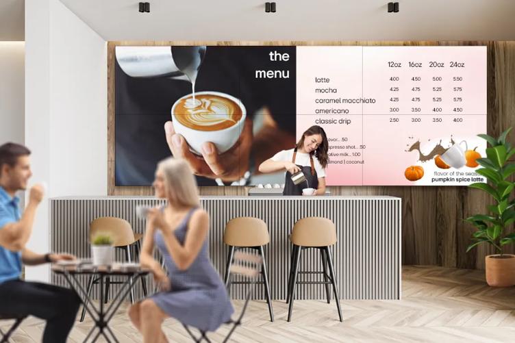 A chic coffee shop with LG video wall behind the counter, displaying the menu and a close-up image of a barista of pouring a latte.
