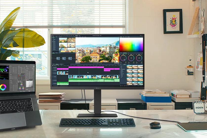 A creative workspace featuring an LG monitor and a connected laptop, both displaying a video editing interface with color grading tools and a timeline.