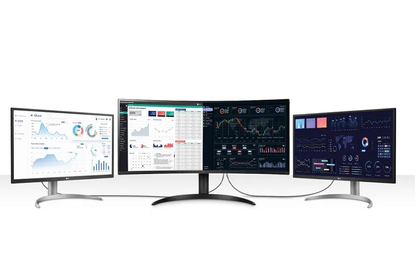 Three monitors displaying various charts and graphs, with the central monitor being curved.