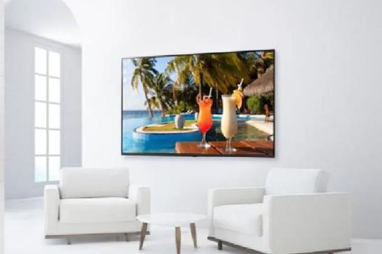 A minimalist living room with white furniture and a TV displaying cocktails by a pool.