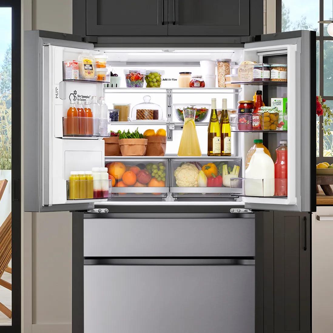 Open, large capacity LG 4-door refrigerator filled with organized fruits, vegetables, bottles, jars, and containers on shelves and drawers under bright light.