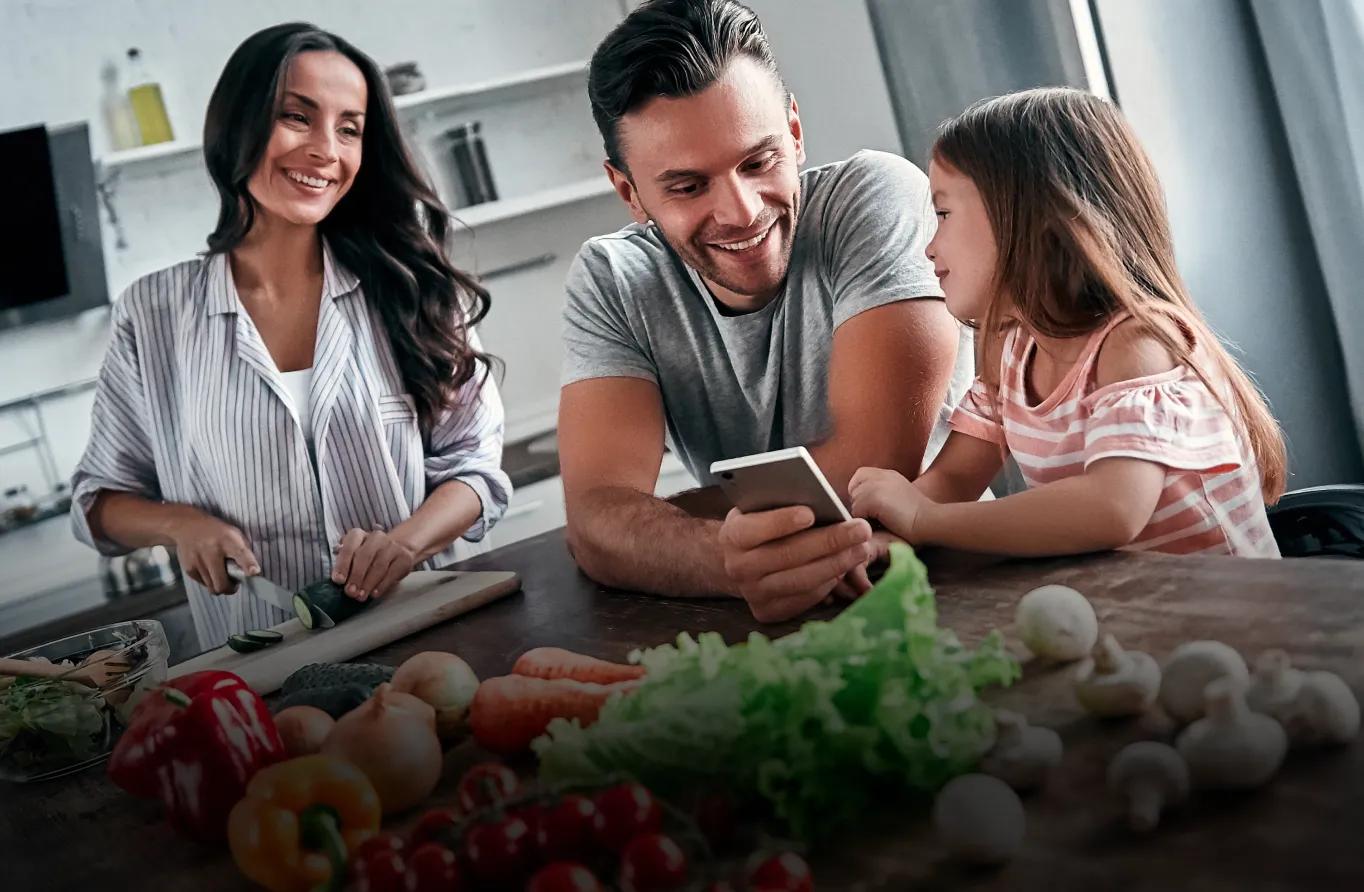 A family preparing food at the kitchen island while looking at the ThinQ recipe on a phone.