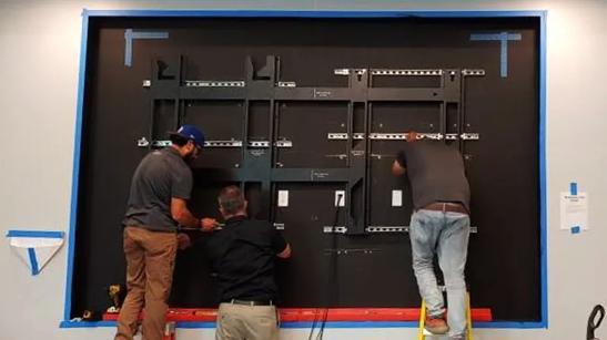 Worker stands on a ladder to install LG Direct View LED modules onto the panel cabinet. 