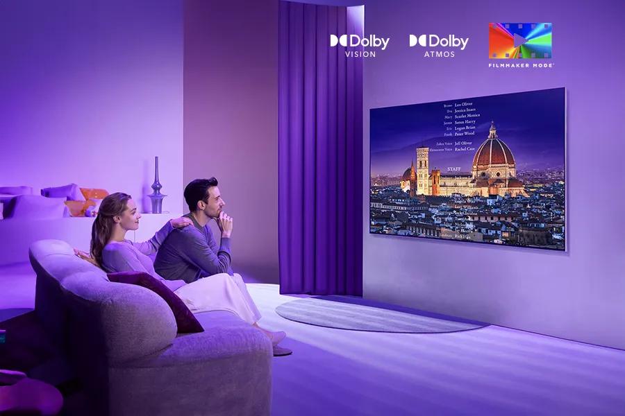 A couple sits on the couch watching a movie on the LG QNED99T with Dolby Vision™, Dolby Atmos® and FILMMAKER MODE™ logos.