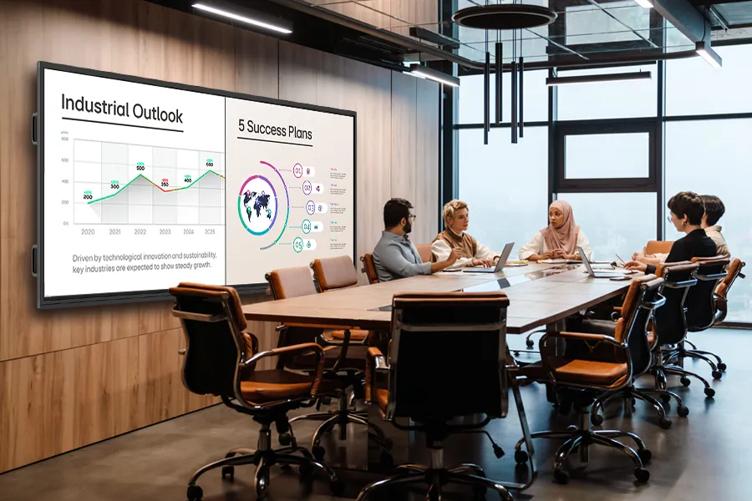 A group of professionals sit in a conference room. A 105-inch CreateBoard is on the wall, showing business data.