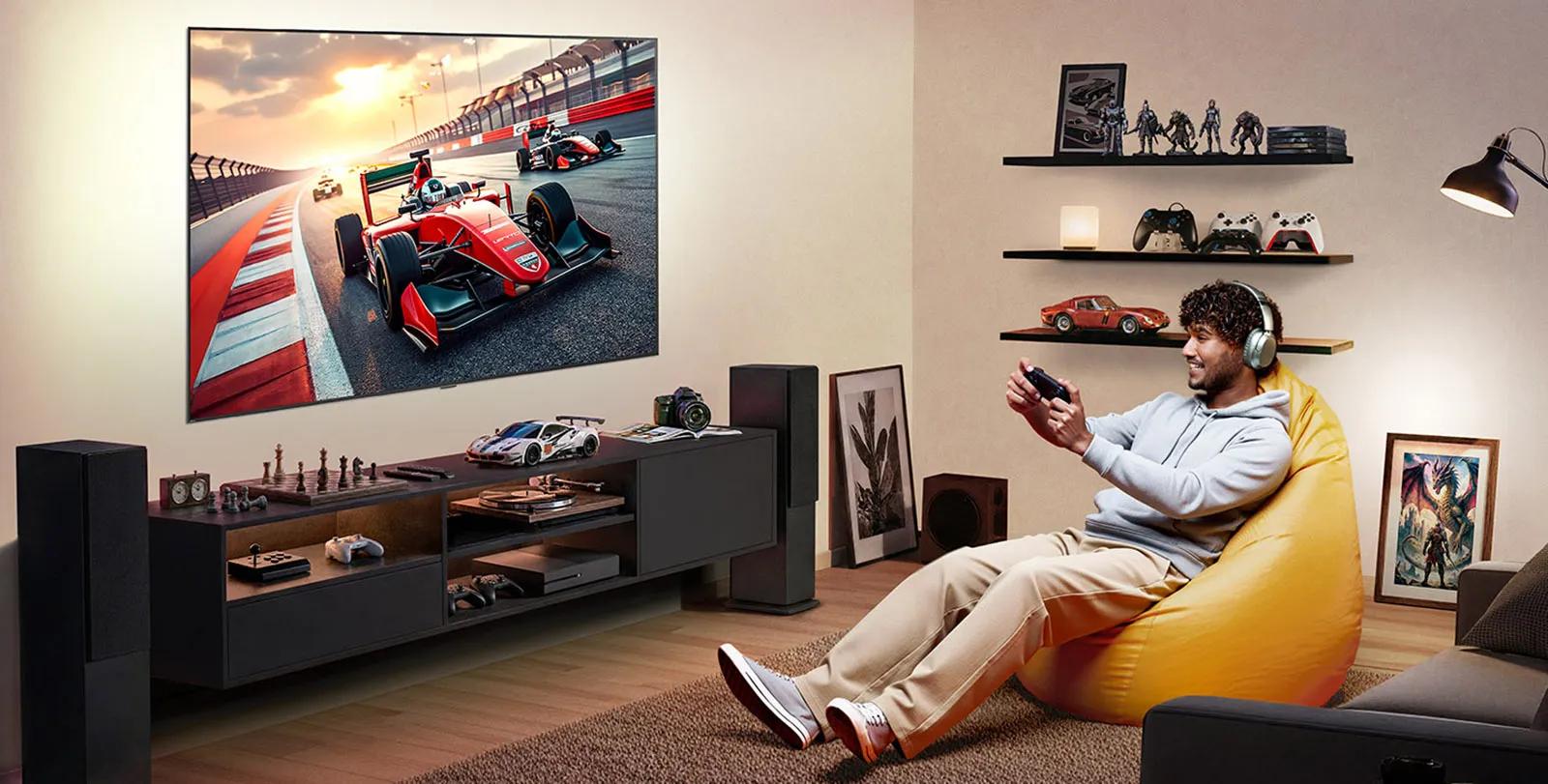 LG TV with big-screen is wall-mounted in a gaming room with gaming gear accents, where a large display shows a high-speed racing scene as a person relaxes on a beanbag, delivering immersive entertainment.