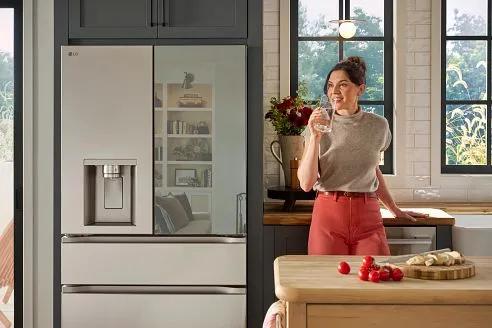 Woman in a kitchen drinking a glass of water in front of an LG MyColor Mirror 4-Door French Door refrigerator.