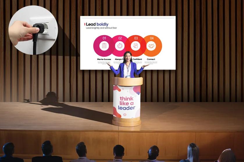 A woman in business dress stands onstage behind a podium. A graphic on the podium reads 'think like a leader.' Behind her is LG All-in-One DVLED LAPA signage, displaying a brightly colored business presentation. A cut-out image circle to the display's left shows a hand plugging in a power connection to a wall socket, indicating LAPA's simple power connection.