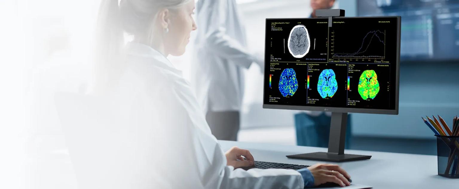A medical professional looks at a monitor displaying brain scans in a clinical setting.