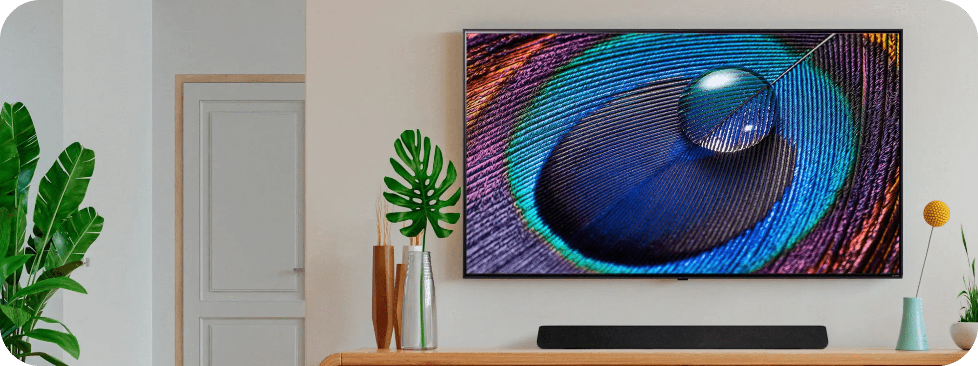 LG TV and Soundbar setup with colorful abstract animation on screen, tropical plants, and a bright modern console table.