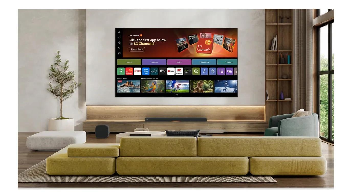 Wall-mounted LG TV displaying the webOS home screen with LG Channels promo, category tabs (Sports, Gaming, Music, Home Hub, Learning), app icons, and recommended content rows, paired with a soundbar and subwoofer, in a modern living room with a mustard-yellow sectional sofa, wood shelving, and a potted plant.