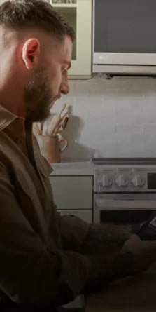 A man sitting in the kitchen using the ThinQ app on is phone to scan the bar code of a frozen meal - tablet.