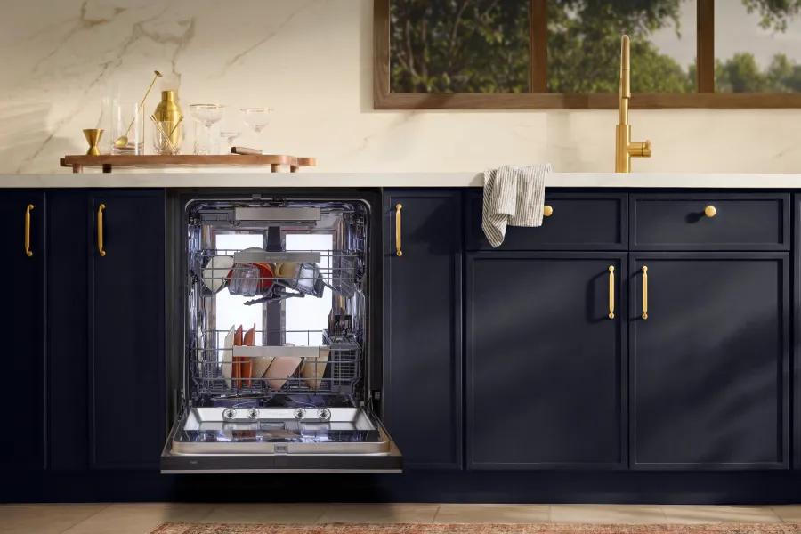 An open, built-in LG dishwasher filled with dishes, integrated into dark navy blue kitchen cabinetry with elegant gold hardware and a white marble countertop.