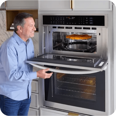 A man opens the upper door of an LG wall oven to check on a freshly baked pizza.