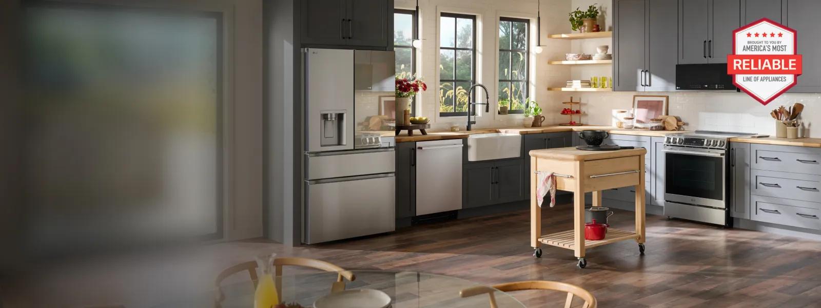 Modern kitchen interior featuring a stainless steel French-door refrigerator, gray cabinetry, open wood shelving with dishes and plants, a farmhouse sink under a window, and a small rolling kitchen island on hardwood floors. Natural light fills the space, creating a clean, warm, and organized atmosphere. A red hexagonal badge reads 'Brought to you by American's Most Reliable Line of Appliances' with five red stars at the top.