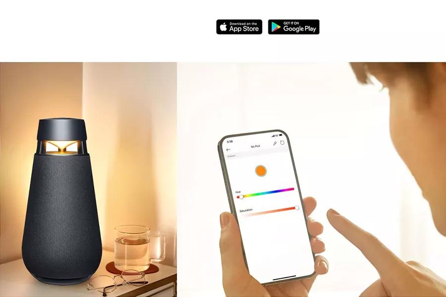 The XBOOM 360 Speaker on a table beside a cup of tea and a pair of glasses while a person controls the color of the light on the speaker from their phone.