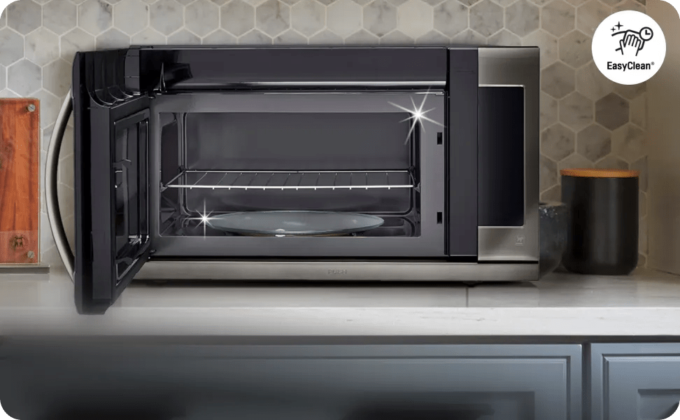 Open LG microwave interior on a counter, showing the clean cavity, glass turntable and door with vents, set against a light tile backsplash.