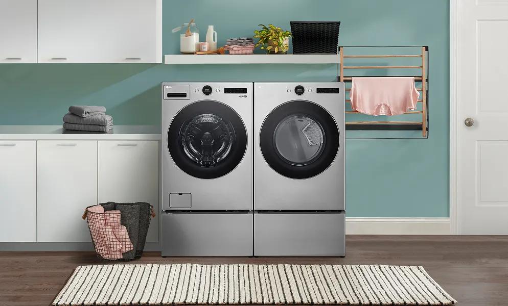 A graphite LG front load washer and LG front load dryer are in a laundry room with white cabinetry and teal walls.