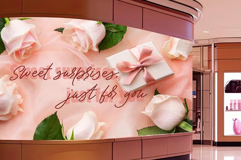 A shopping mall display showing pale pink roses, a gift box, and the text "Sweet surprises, just for you."