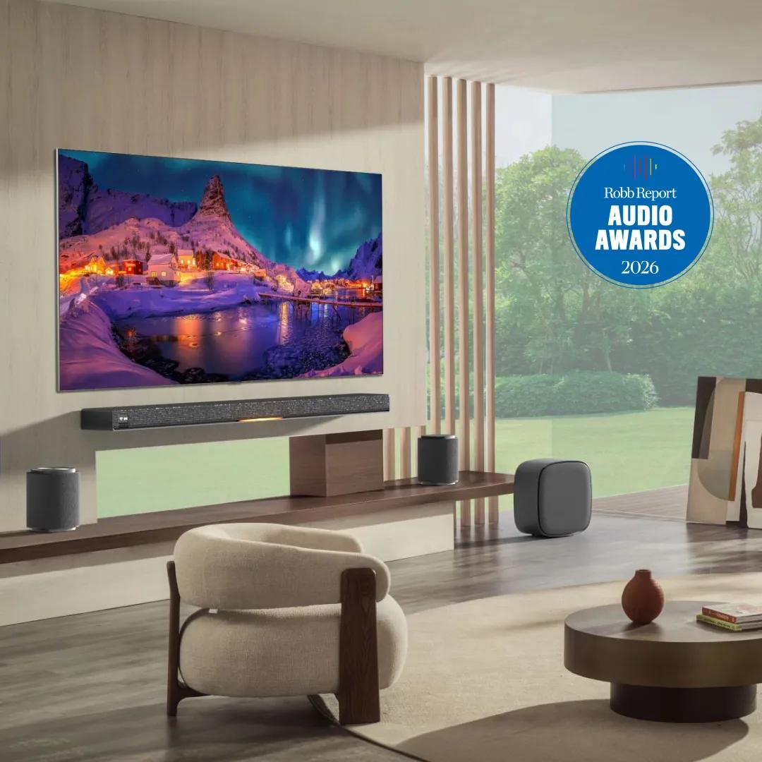 LG OLED TV and soundbar system displayed in a minimalist living room showing a snowy Nordic village with northern lights, flanked by wireless rear speakers and a subwoofer, with a Robb Report Audio Awards 2026 badge.