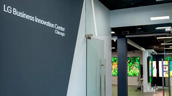 The entrance to LG's  Chicago Business Innovation Center, with the name of the BIC on the wall to the left leading to a pair of open glass doors. Through the doors, glimpses of brightly colored signage can be seen inside of the BIC. 