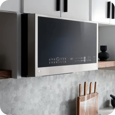 Angled view of an LG over-the-range microwave with a glossy glass door and touch panel, mounted beneath cabinets over a gray tile backsplash.