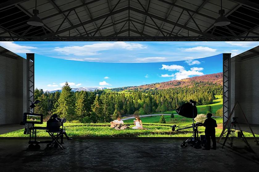 Studio with large LED screen showing a countryside scene and film crew in front.