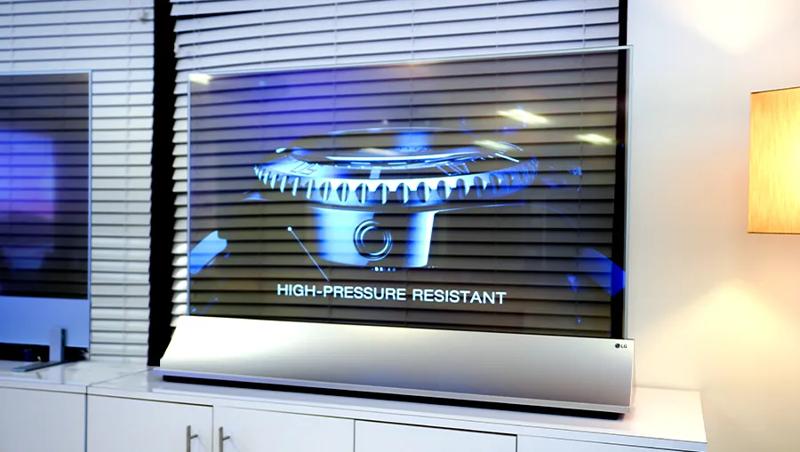 LG transparent OLED signage stands on a display shelf in the LG Atlanta Business Innovation Center. Its display shows a close-up of a luxury watch. The windows behind it are visible through the transparent pane.