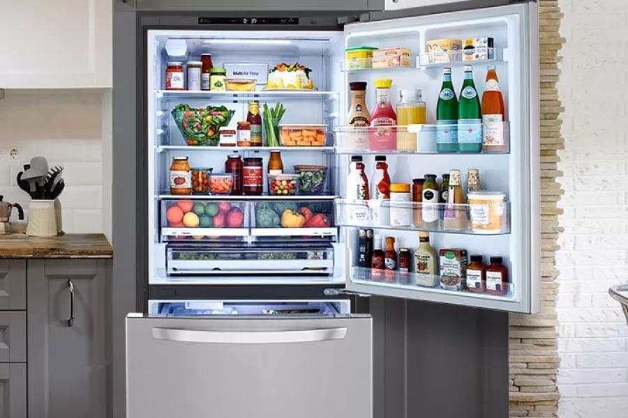 Open LG refrigerator filled with food highlighted by light in a kitchen