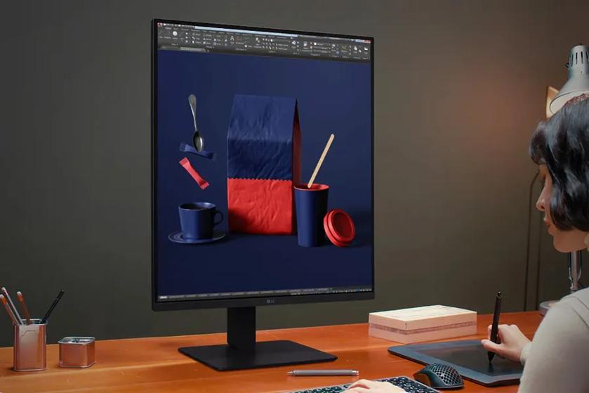 Person working at a desk with a large monitor displaying 3D-rendered objects.