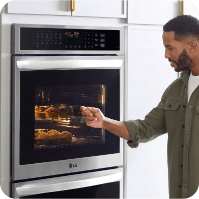 A man checks a tray of muffins baking in an LG double wall oven.