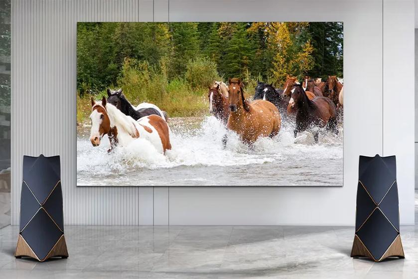 A large screen showing horses running through a river, flanked by geometric black and gold speakers.