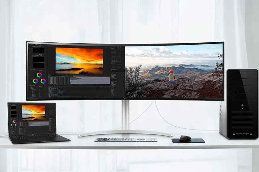 A workspace with a curved monitor, laptop, and desktop tower on a white desk.