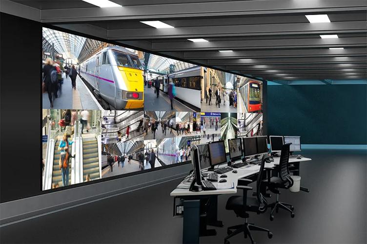 Control room with a large wall-mounted display of train station surveillance images.