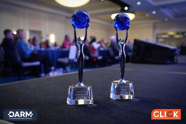 Two silver trophies with blue globes on a stage at a conference with an audience in the background.
