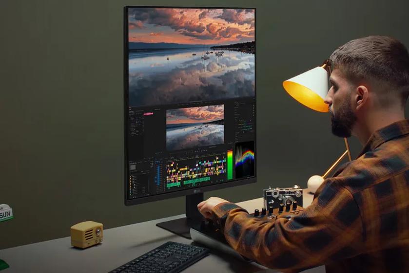 A person editing video on a vertical monitor with a control panel, a vintage radio, and a desk lamp.