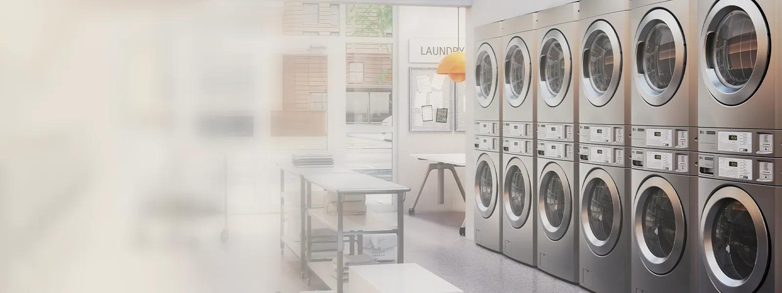 LG commercial laundry room with stacked front-load washers and dryers lining the wall, folding tables visible nearby