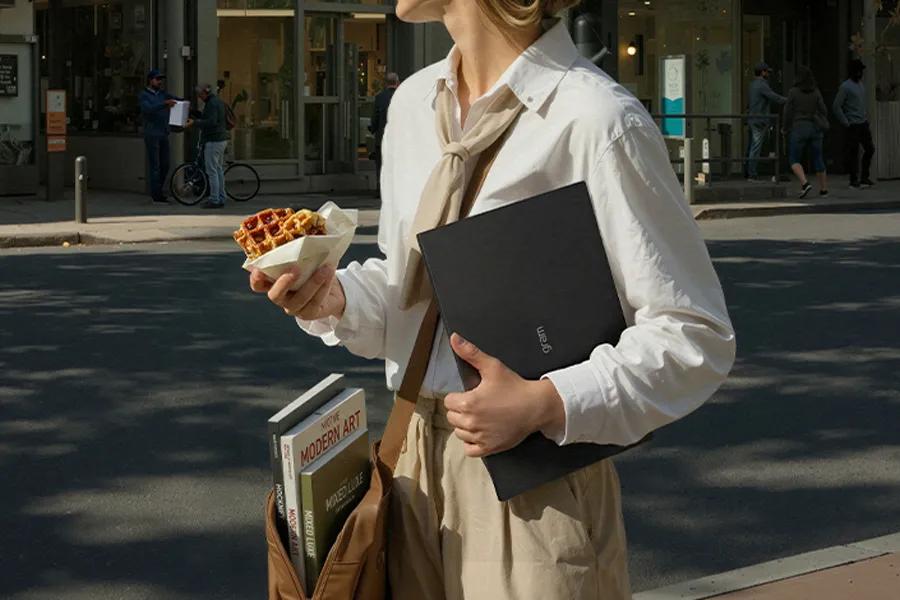 LG gram 15Z95U-G-AU87U1 laptop shown in sleek black design held by person in white shirt with books and waffle snack on city street