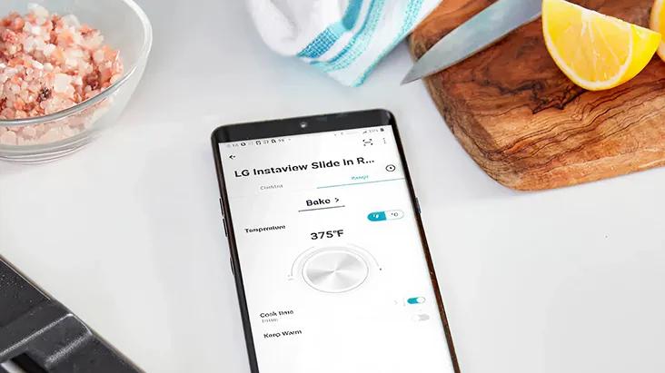 A smartphone displays the LG ThinQ app controlling the LG InstaView Slide-In Range oven, enabling efficient product maintenance in the kitchen.