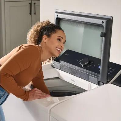 Woman removing laundry from a white top-load washer.