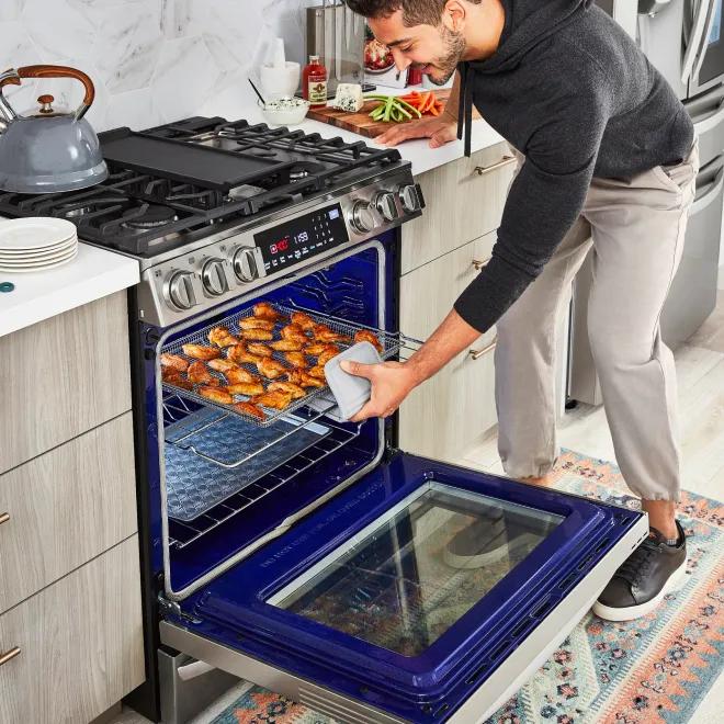 Man pulling out a tray of chicken wings from an LG range oven.