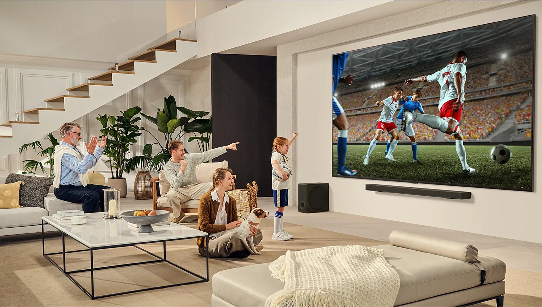 Family gathered in bright living room cheering while watching live soccer match on a large wall-mounted LG TV.